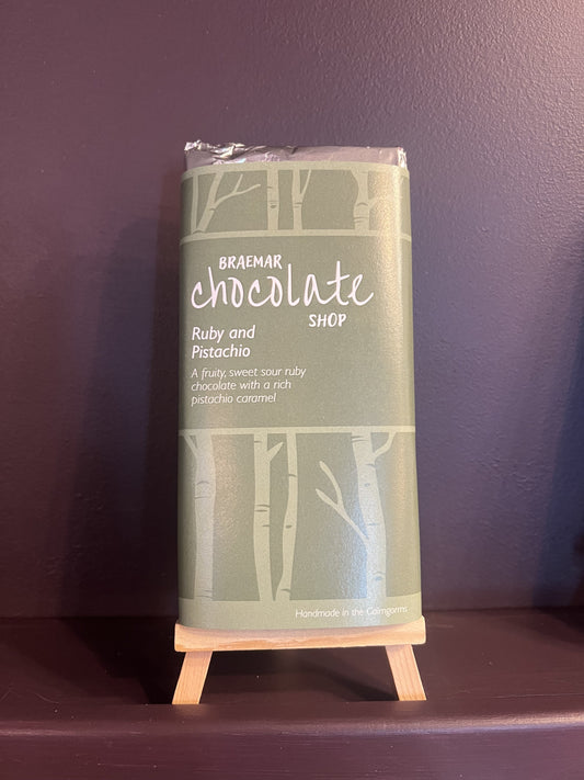 A wrapped chocolate bar from Braemar Chocolate Shop, labeled Ruby and Pistachio, resting on a dark purple textured surface.